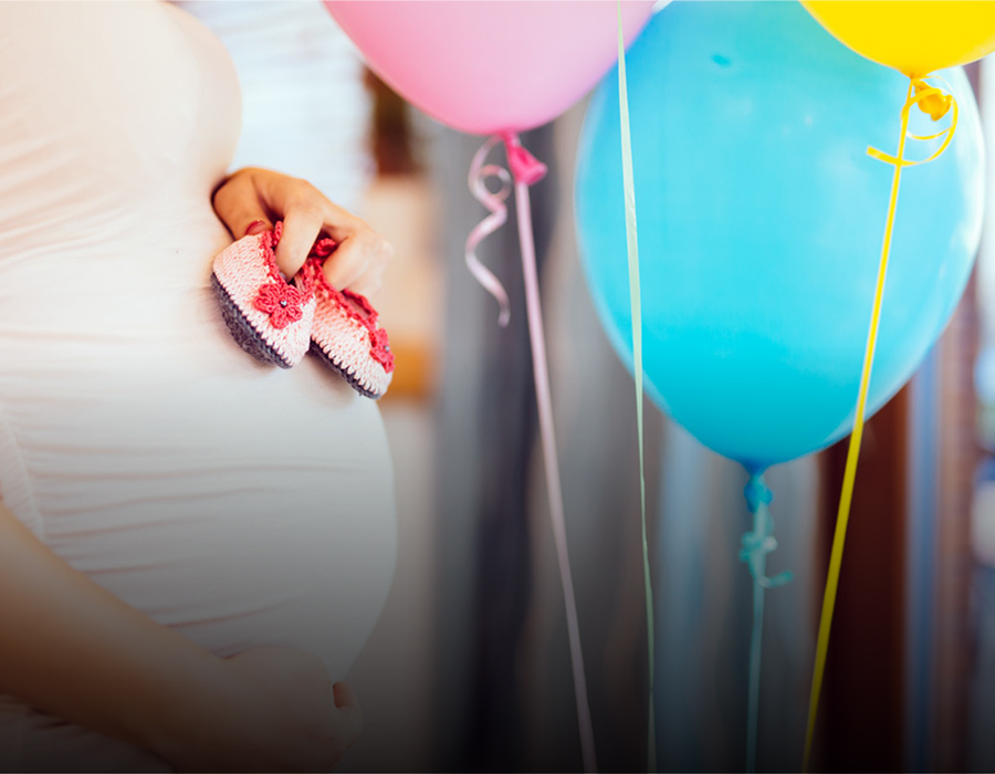 A tender moment during pregnancy, with a person holding tiny baby shoes, surrounded by pink and blue balloons, suggesting anticipation for the baby's arrival.